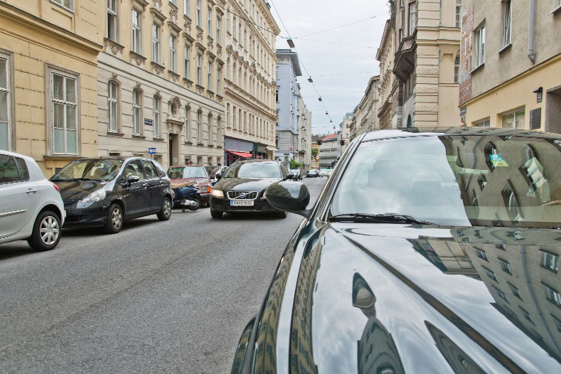 Auf diesem Bild sehen Sie die Situation aus der Perspektive eines größeren zehnjährigen Kindes. Es kann sich aufgrund der höheren Körpergröße und des dadurch bedingten höheren Blickstandorts bereits einen guten Überblick verschaffen, es kann alle für eine sichere Querungsentscheidung relevanten Verkehrsdetails wahrnehmen. Auch der Autofahrer oder die Autofahrer:in kann das größere Kind einfacher wahrnehmen, sein Kopf ist deutlich über dem Seitenspiegel des parkenden Kfz.