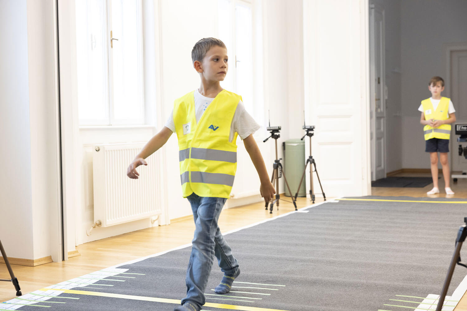 Kleines Kind mit Warnweste, das über einen Straßenteppich geht