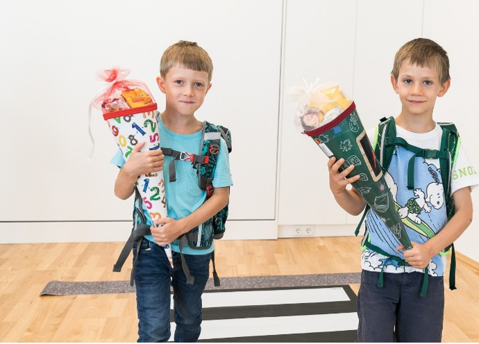 Zwei Schulkinder stehen auf einem Zebrastreifen-Teppich mit ihren Schultüte
