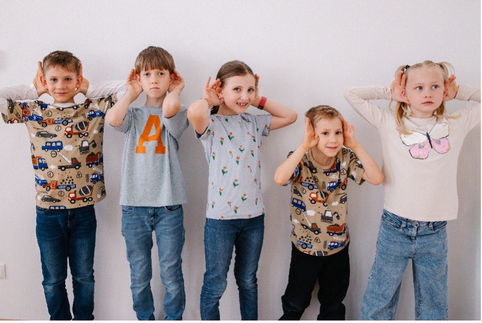 Fünf Kinder stehen nebeneinander und halten sich die Hände an die Ohren, um Verkehrsgeräusche bewusst wahrzunehmen.