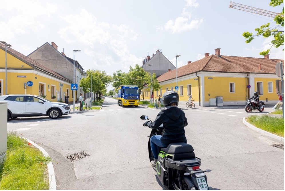 Aus Sicht der*m Mopedfahrer:in steht man an einer Ampelkreuzung mit wartenden Auto- und Lkw-Fahrenden sowie einer Motorradfahrer:in. Die Mobilitäts-App soll die Perspektiven der unterschiedlichen Verkehrsteilnehmer:innen , aus unterschiedlichen Richtungen kommend, verdeutlichen.