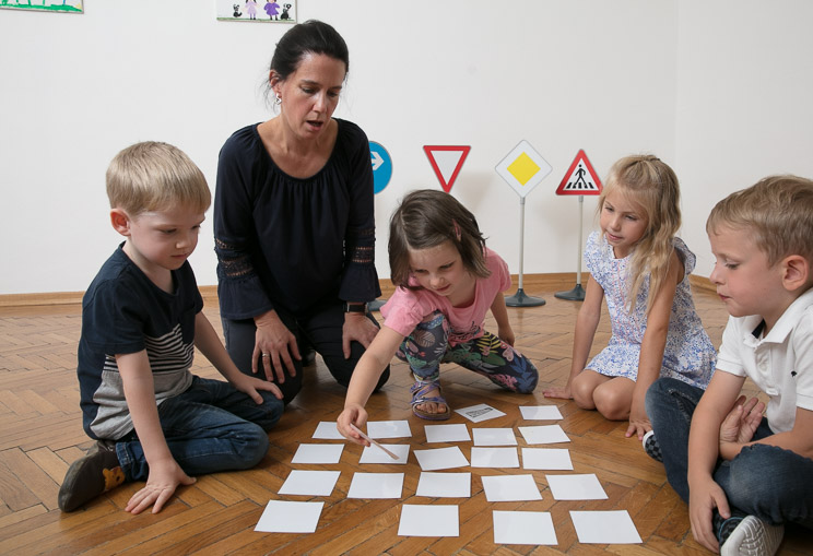 Eine Verkehrstrainerin führt mit drei Kindern im Alter von 1 bis 3,5 Jahren einen Verkehrssicherheits-Workshop für Tagesmütter und -väter durch.