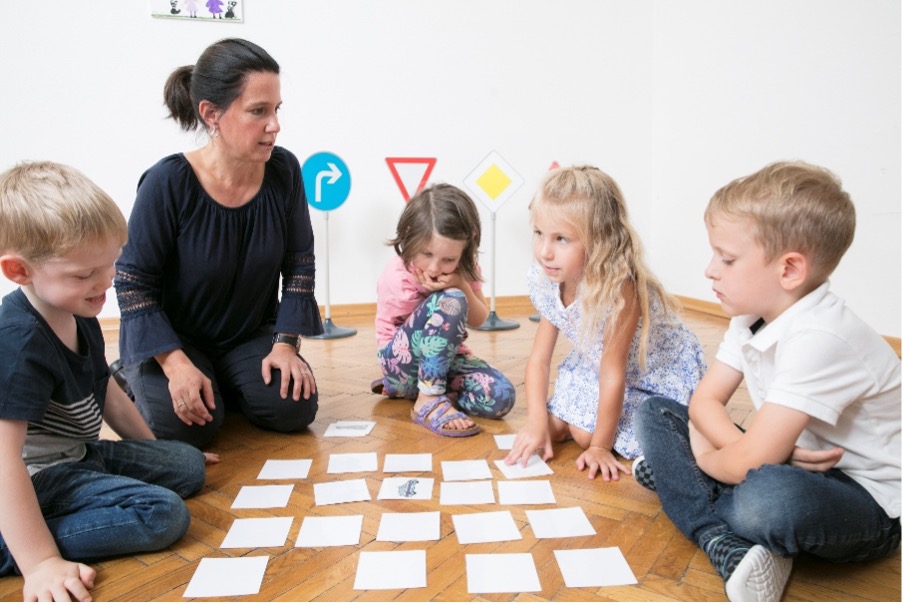 Eine Verkehrstrainerin führt mit drei Kindern im Alter von 1 bis 3,5 Jahren einen Verkehrssicherheits-Workshop für Tagesmütter und -väter durch.
