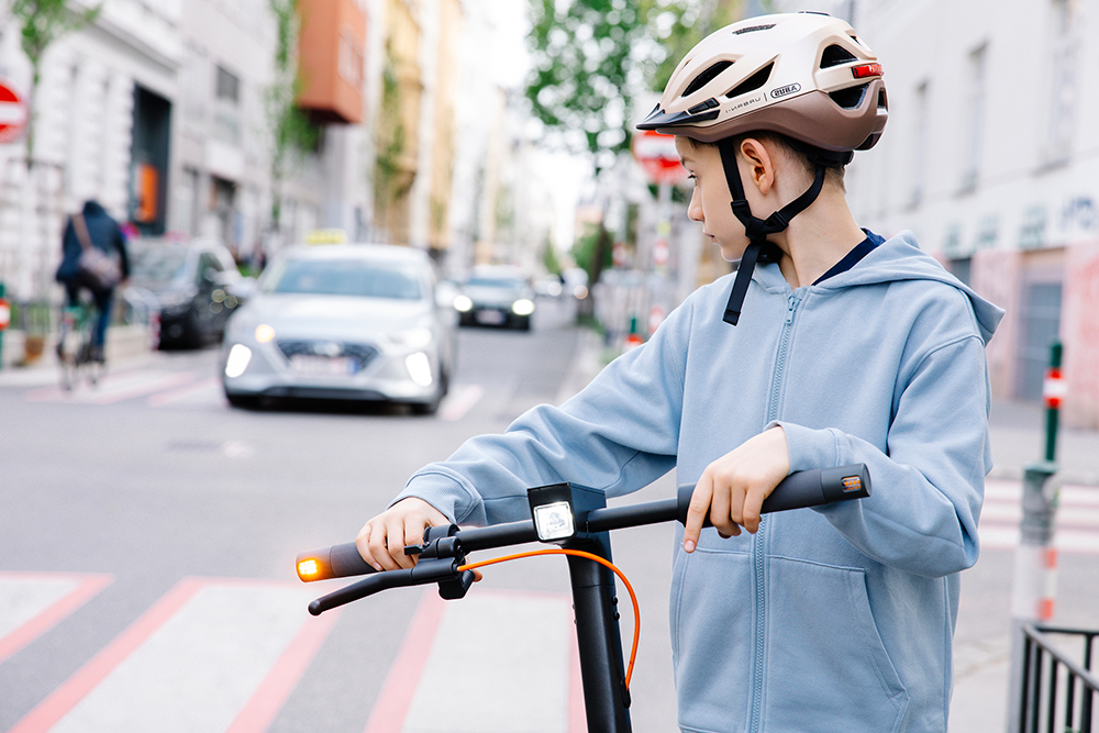 Junge mit Scooter blickt nach hinten auf Fahrbahn