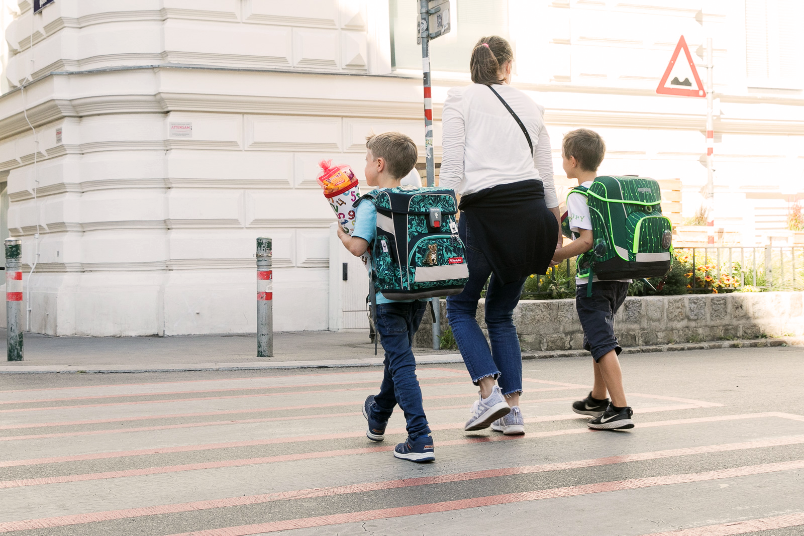 Eine Mutter begleitet zwei Schulkinder beim Überqueren eines Zebrastreifens.