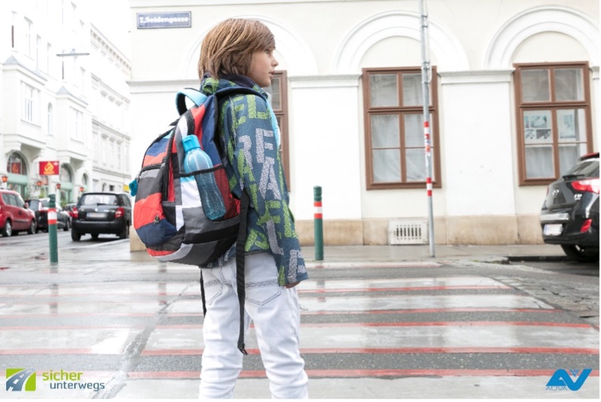 Schulkind steht an Zebtrastreifen und blickt nach rechts.