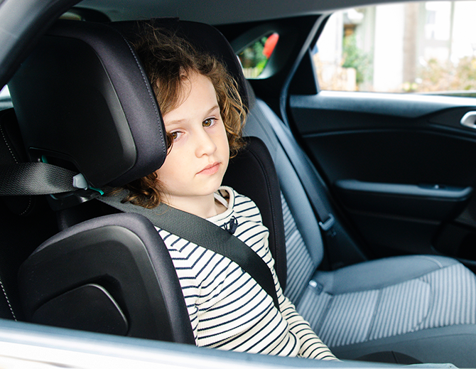 Ein Kind sitzt angeschnallt in einem Kindersitz auf der Rückbank eines Autos.
